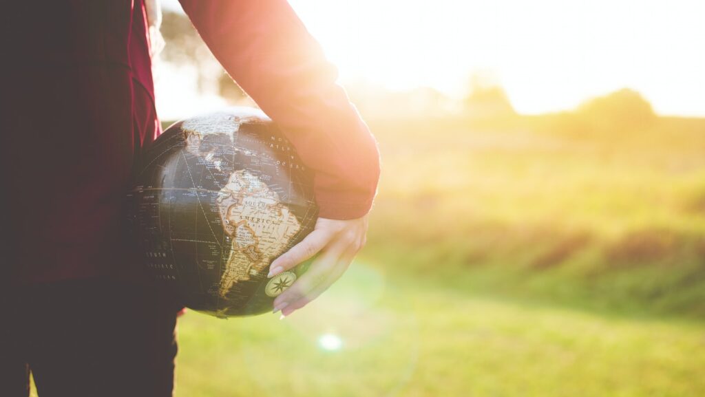 person holding black and brown globe ball while standing on grass land golden hour photography